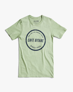 The Cafe Gitane classic t-shirt in green is printed with the logo in a stamped structure. The print ins circular in the middle of the front chest and in navy blue. The logo features each city Cafe Gitane has a location in: New York, Los Angeles, and Tokyo, as well as when the first location opened: 1994. 