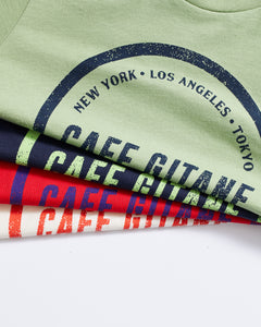 Alt Text: The Cafe Gitane Stamped Logo Tee is 100% organic cotton and made in the USA. The classic t-shirt come in green, red , navy, and natural and is printed with the logo in a stamped structure. The print ins circular in the middle of the front chest. The logo features each city Cafe Gitane has a location in: New York, Los Angeles, and Tokyo, as well as when the first location opened: 1994. 